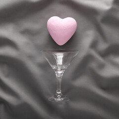 Cocktail glass with heart on gray crumpled silk background. Party concept