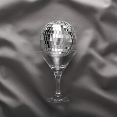Cocktail glass with disco ball on gray crumpled silk background. Party concept