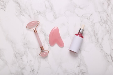 Jade massage roller with guasha stone and serum bottle on marble background