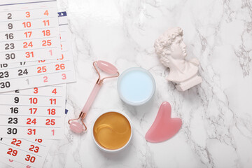 Cosmetic products for facial skin care and David bust, calendar on a marble background. Flat lay