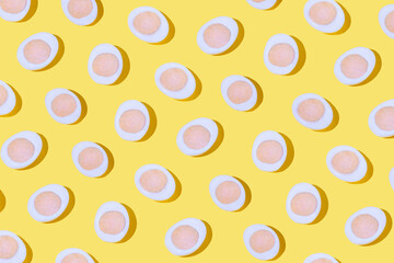 Creative pattern with sliced eggs on bright yellow background. Trendy breakfast wallpaper.