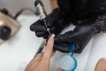 Manicure master removes cuticles with electric file machine on female hand in nail salon