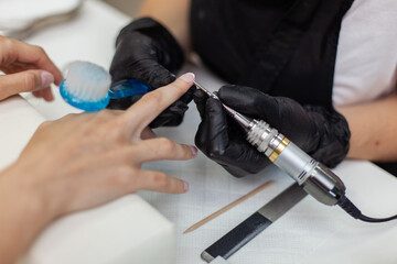 Manicure master removes cuticles with electric file machine on female hand in nail salon