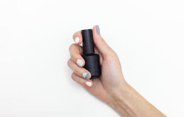 Fototapeta premium Woman's hand holding a black bottle of nail polish on a white background