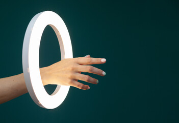 Woman's hand through a glowing circle ring lamp on a green background