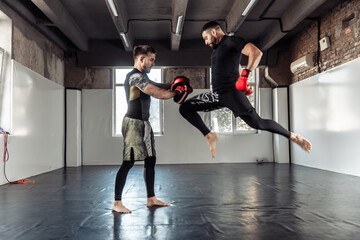 Male fighter training kicks with partner with training boxing paws