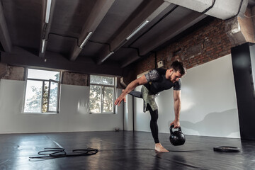 Fototapeta premium Young athletic man exercising with a kettlebell in a gym