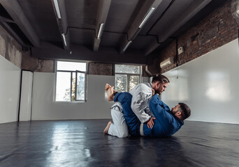 Two fighters sparring a partner in a kimono are training painful holds in a sports hall