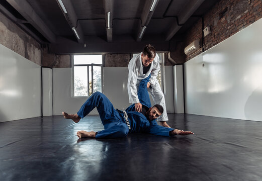 Two fighters sparring a partner in a kimono are training painful holds in a sports hall