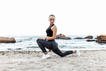 Fototapeta na wymiar Beautiful young fit woman in sportswear practicing stretching legs alone on wild beach. Healthy lifestyle concept