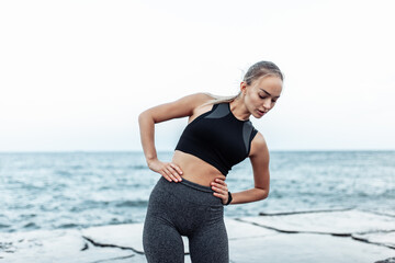 Beautiful young fit woman in sportswear training alone on urban beach. Healthy lifestyle concept