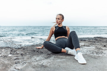 Fototapeta na wymiar Fit woman in sportswear sitting on urban beach
