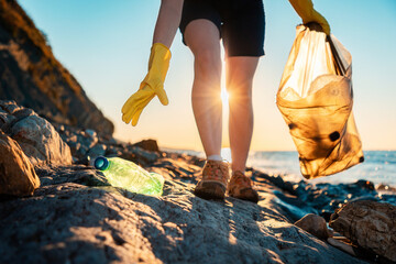 Global environmental pollution. A volunteer collects plastic bottles on the ocean shore. Legs close-up. Cleaning of the coastal zone. The concept of environmental conservation