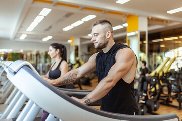 Athletic man and woman exercising together, running on treadmill in the gym