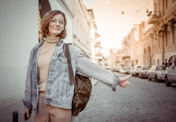 Stylish attractive woman in denim jacket catches car with thumbs up gesture on urban street
