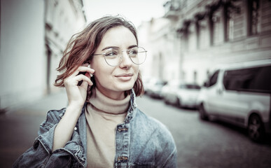 Portrait of a charismatic stylish and modern woman in trendy clothes with glasses and headphones. Attractive young woman walking along the urban street