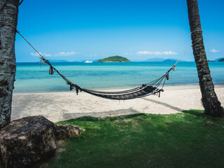 Obraz premium Relax beach hammock on peaceful white sand beach tropical island with clear turquoise sea against blue sky with Koh Kham view at horizon. Koh Mak Island, Trat, Thailand.