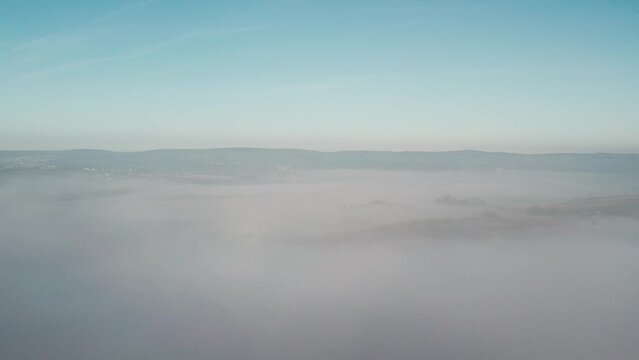 AERIAL: Slow rise up through cloud inversion revealing valley and hills covered in fog, Gower, 4k Drone