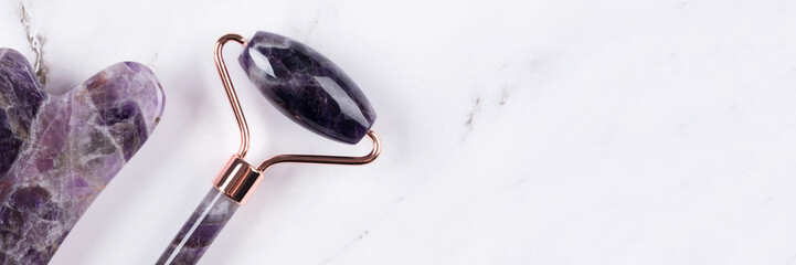 Banner with facial massage kit - amethyst gua sha tool and face roller on white marble background. Face roller, massager made from natural stones, home spa