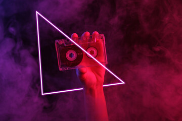 Hand holding audio cassette in dense smoke with red-blue neon light with triangle.