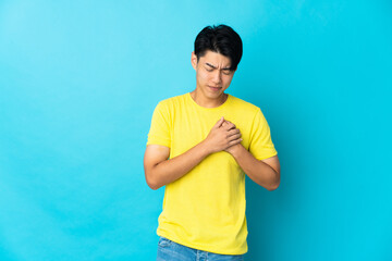 Young Chinese man isolated on blue background having a pain in the heart
