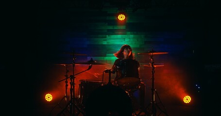 Female drummer with red hair playing on stage during rock show in nightclub
