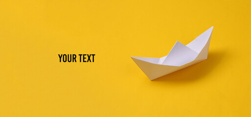 Paper origami boat on yellow background. Space for your text - obrazy, fototapety, plakaty