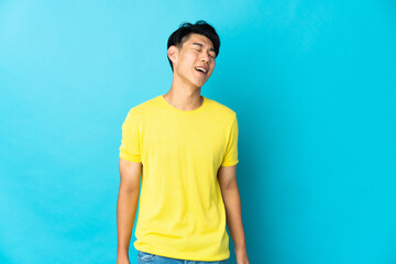 Young Chinese man isolated on blue background laughing
