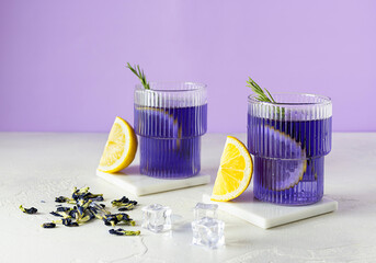 Two transparent glasses of blue iced tea on a bright table