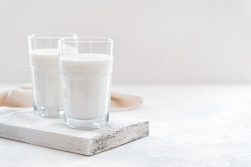 Two glasses of milk on a wooden board on a light background. Side view, copy space.