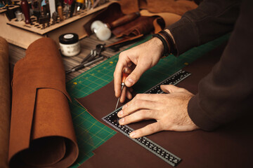 Tanner works with leather, makes purse, manual labor, small business, production. Close up, indoor, lifestyle, authentic atmosphere. leatherworker draws, measures with ruler