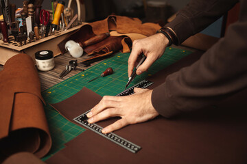 Tanner works with leather, makes purse, manual labor, small business, production. Close up, indoor, lifestyle, authentic atmosphere. leatherworker cuts, ruler - obrazy, fototapety, plakaty