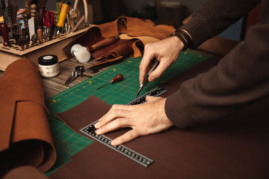 Tanner works with leather, makes purse, manual labor, small business, production. Close up, indoor, lifestyle, authentic atmosphere. leatherworker cuts, ruler