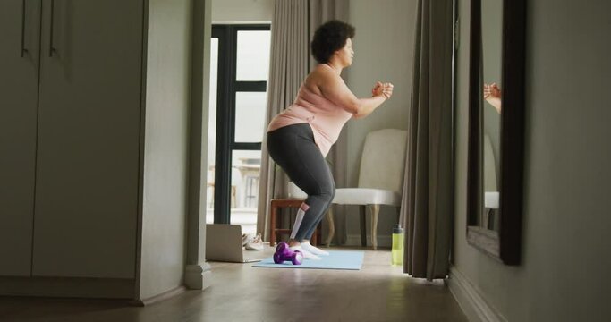 Video of plus size african american woman exercising at home, doing squats