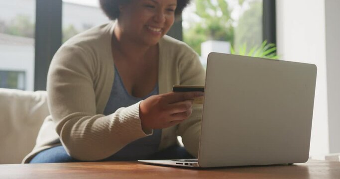 Video of happy plus size african american woman holding credit card and using laptop