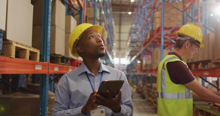 African american male worker with helmet using tablet in warehouse - Powered by Adobe