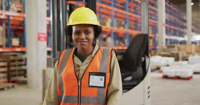 Portrait of african american female worker wearing safety suit and smiling in warehouse