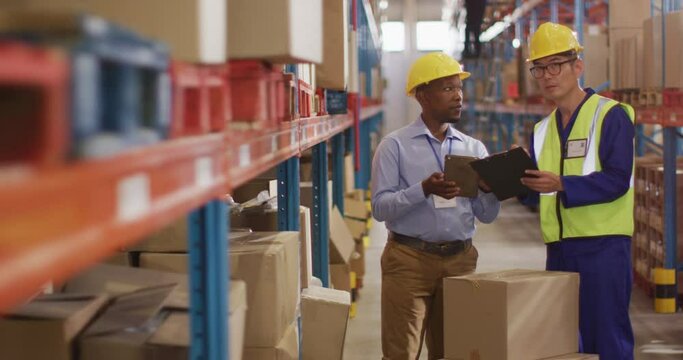 Diverse male workers wearing safety suits and talking in warehouse