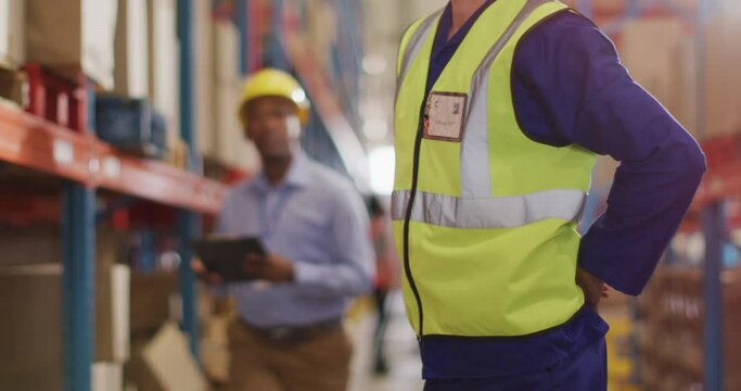Diverse male workers wearing helmet and touching back in warehouse