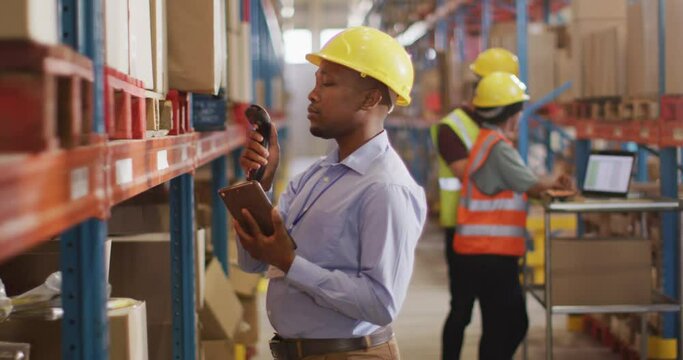 African american male worker with helmet using smartphone in warehouse
