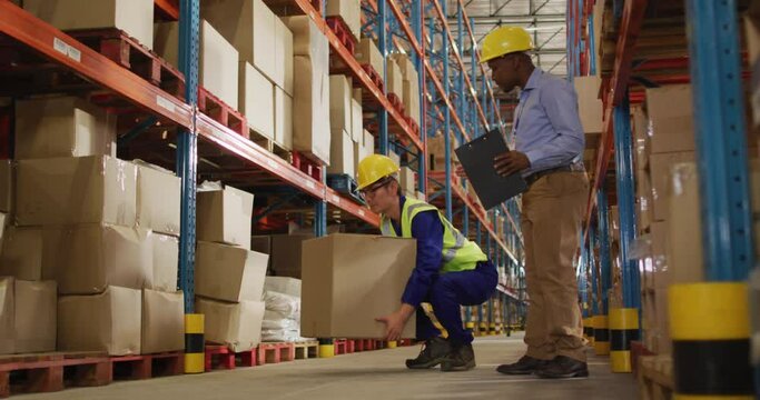 Diverse male workers wearing helmet and carrying boxes in warehouse