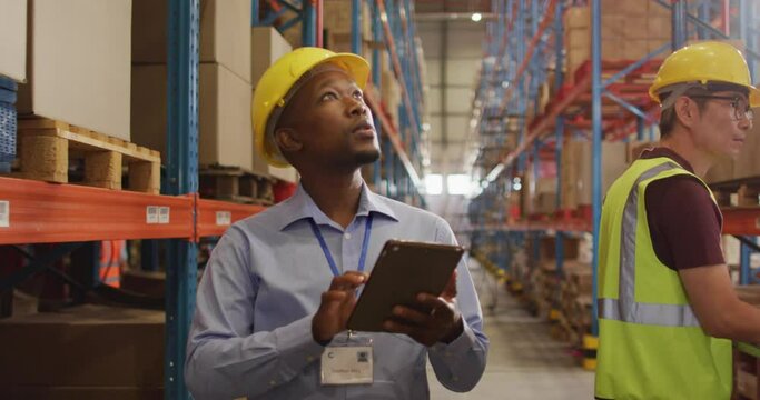 African american male worker with helmet using tablet in warehouse