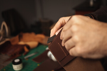 tanner makes genuine leather wallet, professional craftsman, closeup, indoor, authentic, business. Handiwork. treats edges with sandpaper