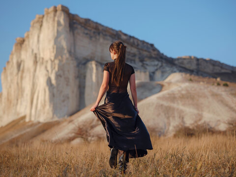 Fashionable woman on desert field near mountain wearing black dress
