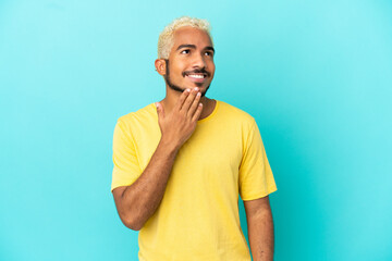 Young Colombian handsome man isolated on blue background looking up while smiling
