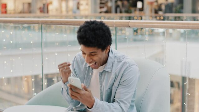 African guy user online betting mobile game win sitting indoors with phone success yes gesture win proposal man receiving sms message offer opportunity with smartphone male winner celebrating victory 