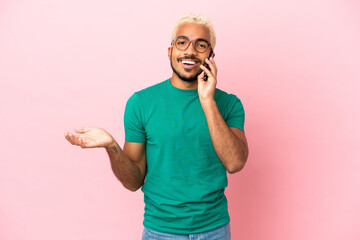 Young Colombian handsome man isolated on pink background keeping a conversation with the mobile...