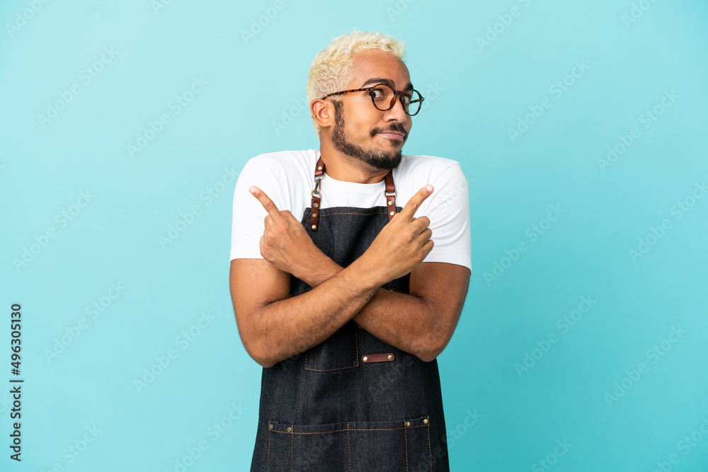 Wall mural restaurant colombian waiter man isolated on blue background pointing to the laterals having doubts