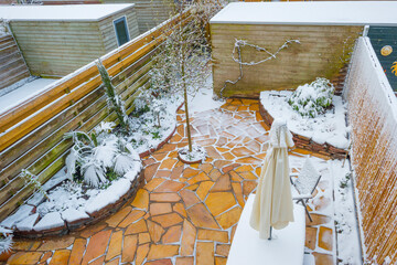 Garden with plants and colorful flagstones surprised by snow in springtime, Almere, Flevoland, The Netherlands, April 1, 2022