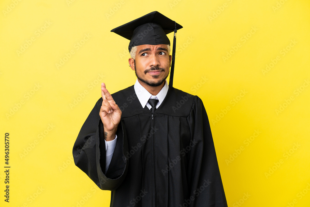 Poster Young university graduate Colombian man isolated on yellow background with fingers crossing and wishing the best